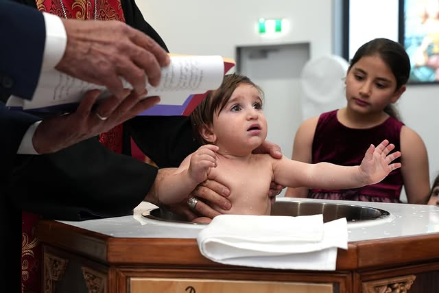 Baby held above the baptismal font
